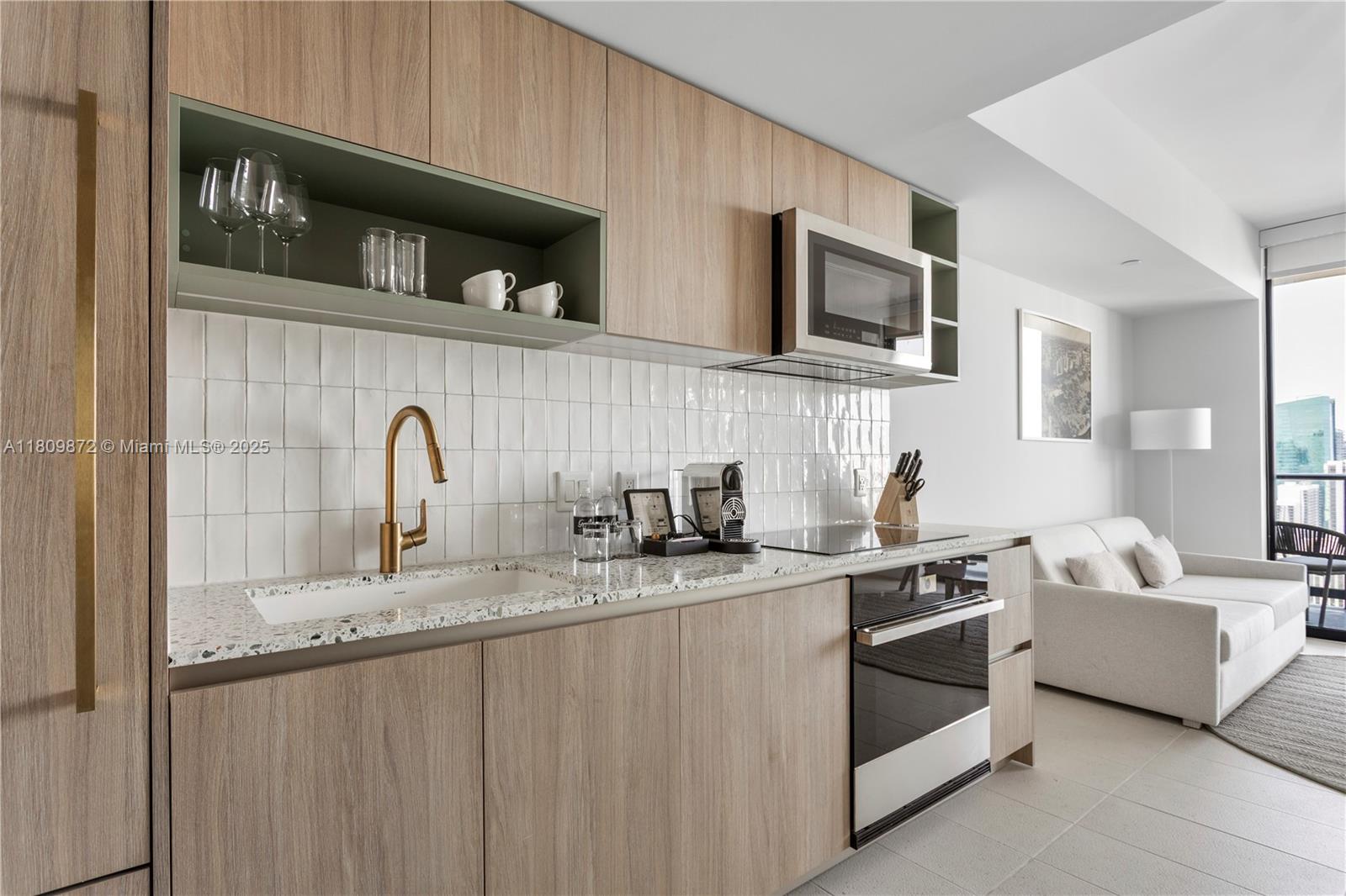 A modern kitchen features light wood cabinetry, white tile backsplash, and a speckled stone countertop — 601 NE 1st St # 3907, Miami FL 33132, MIAMI, FL