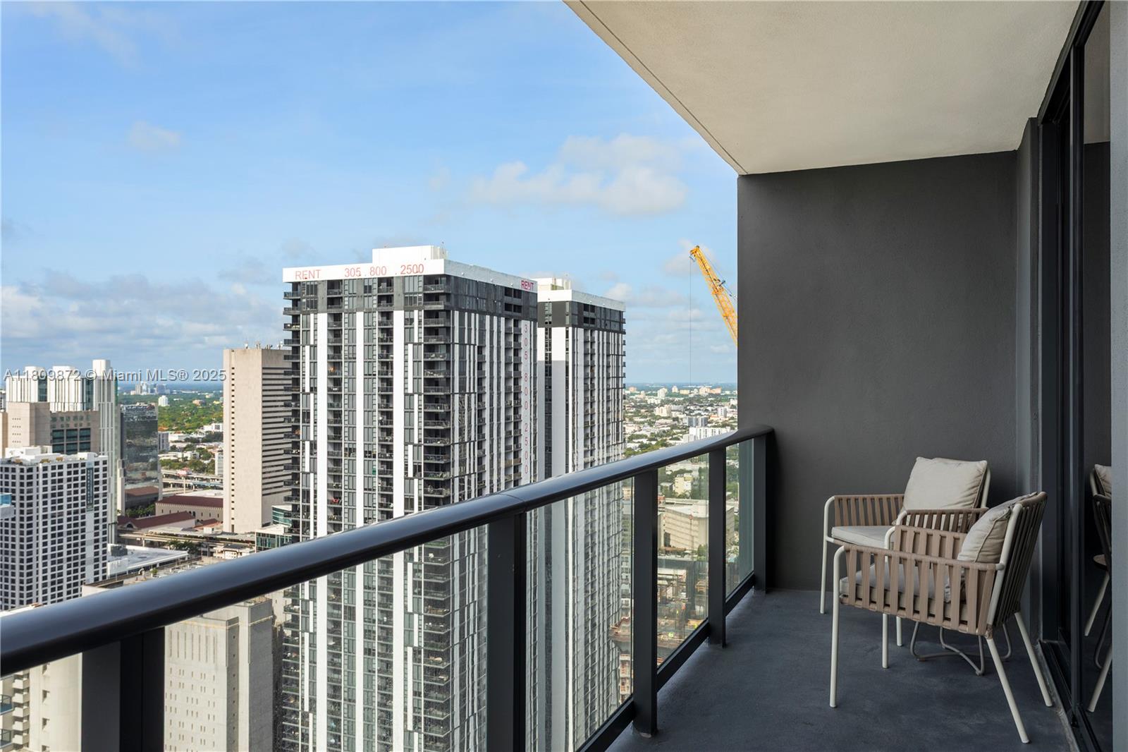 A balcony with two chairs overlooks a city skyline featuring tall residential buildings — 601 NE 1st St # 3907, Miami FL 33132, MIAMI, FL