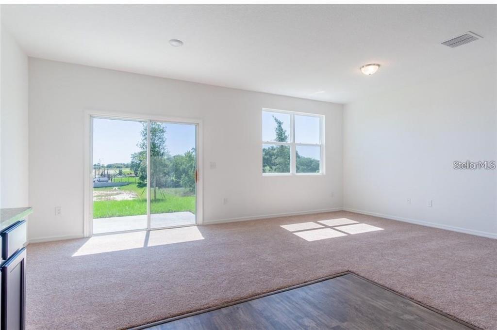 A living area with beige carpet, white walls, a sliding glass door, and a window — 342 MADISON DRIVE, DAVENPORT, FL