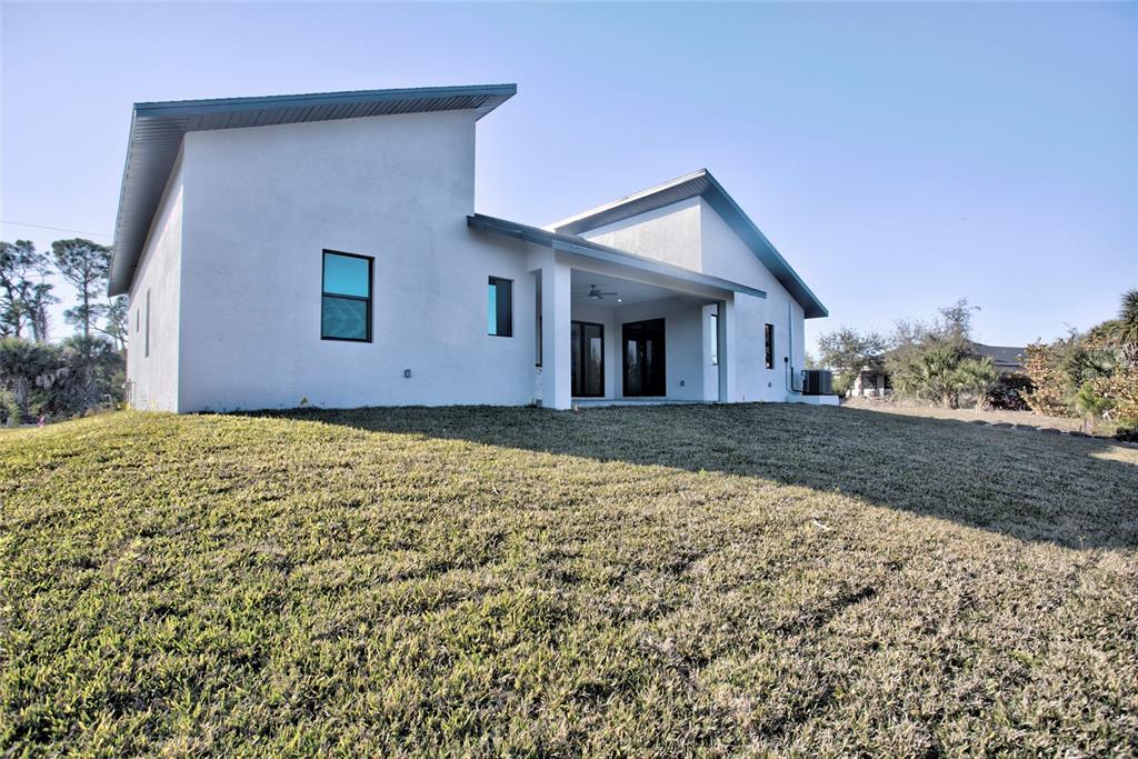 The exterior of a modern white house features a covered patio and a sloped lawn — 9574 SALT LAKE STREET, PORT CHARLOTTE, FL