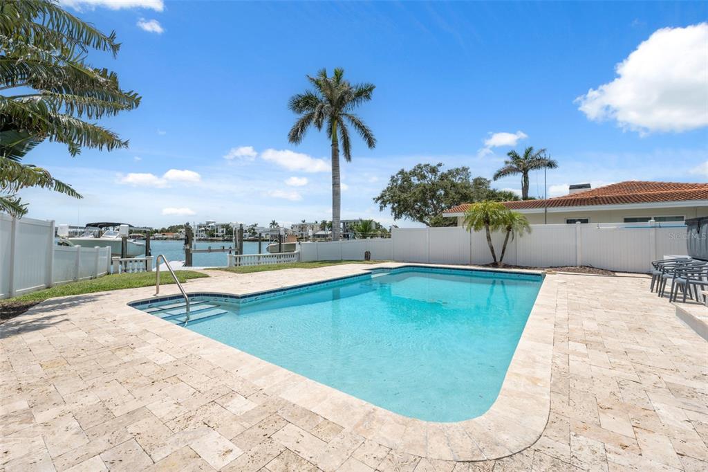 A swimming pool with a stone deck sits in a backyard overlooking a canal — 900 79TH STREET S, ST PETERSBURG, FL