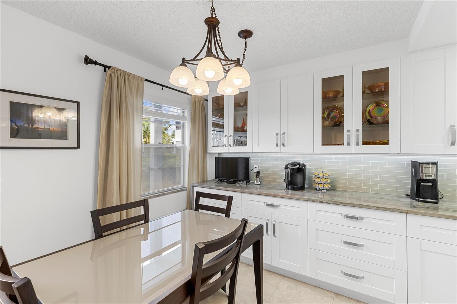 A dining area features a glass-top table, white cabinetry, and a five-light chandelier — 210 Oakridge N # 210, Deerfield Beach FL 33442, DEERFIELD BEACH, FL