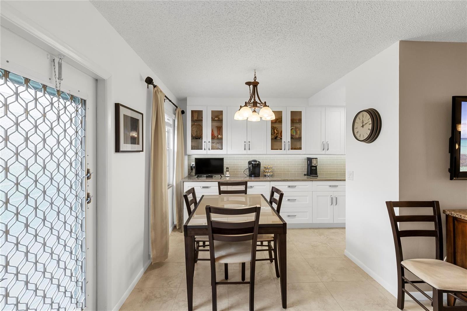 A dining area features a glass-topped table, dark wood chairs, white cabinetry, and tile flooring — 210 Oakridge N # 210, Deerfield Beach FL 33442, DEERFIELD BEACH, FL