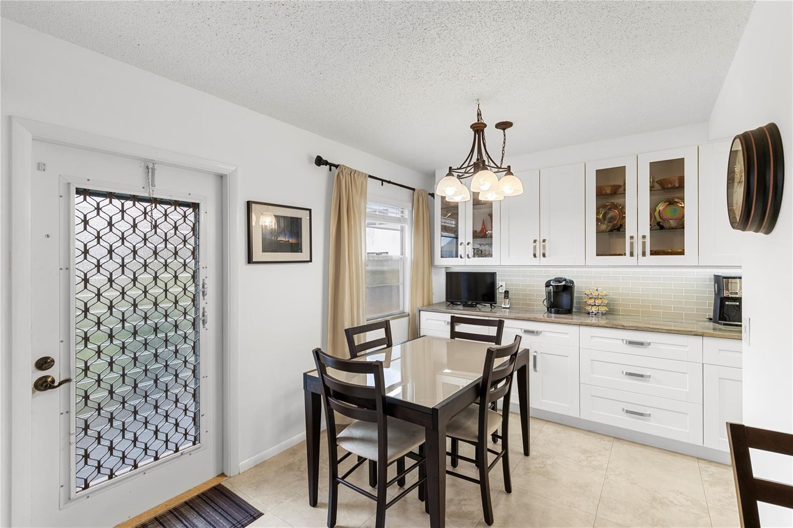 A dining area features a glass-topped table, white cabinetry, a chandelier, and a security door — 210 Oakridge N # 210, Deerfield Beach FL 33442, DEERFIELD BEACH, FL