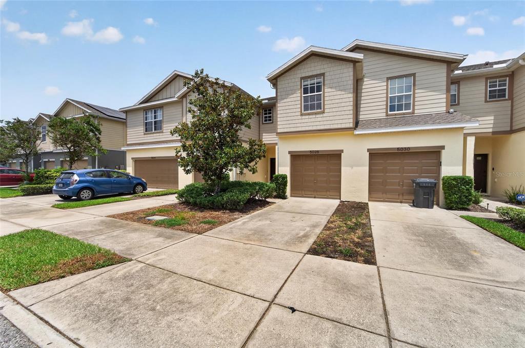 A row of two-story townhomes with tan siding, brown garage doors, and concrete driveways — 5028 WHITE SANDERLING COURT, TAMPA, FL