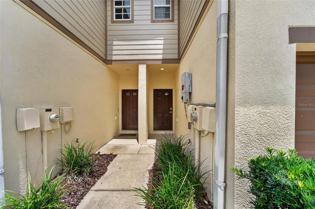 A concrete walkway leads to two brown front doors between beige exterior walls — 5028 WHITE SANDERLING COURT, TAMPA, FL