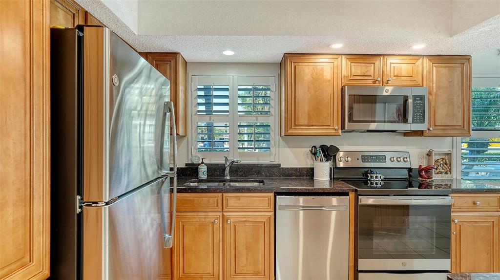 A kitchen features stainless steel appliances, wood cabinets, and dark countertops — 1001 BENJAMIN FRANKLIN DRIVE UNIT 110, SARASOTA, FL