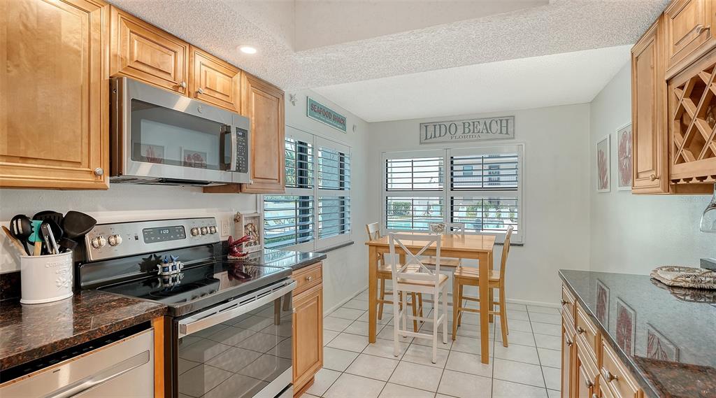 A kitchen features light wood cabinets, dark granite countertops, stainless steel appliances, and a dining area — 1001 BENJAMIN FRANKLIN DRIVE UNIT 110, SARASOTA, FL