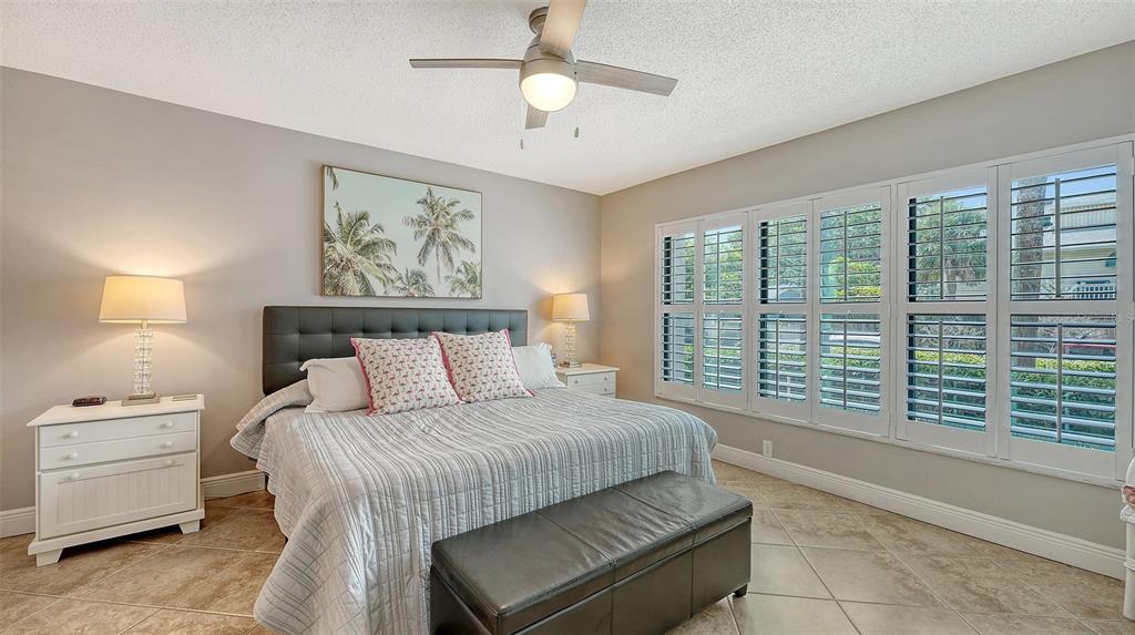 A bedroom features a king bed, white nightstands, plantation shutters, and light-colored tile flooring — 1001 BENJAMIN FRANKLIN DRIVE UNIT 110, SARASOTA, FL