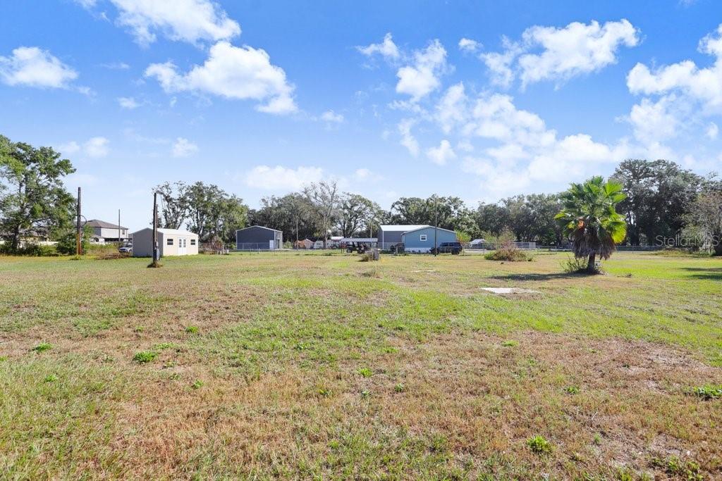A large, grassy, vacant lot features a few small outbuildings and trees under a blue sky — 4005 SW TIMBERWOOD DRIVE, LAKELAND, FL