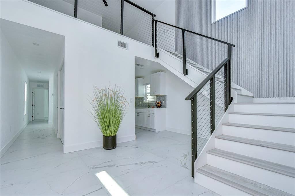 A modern entryway features white marble floors, a staircase with cable railings, and a kitchen view — 222 8TH AVENUE DRIVE W, BRADENTON, FL