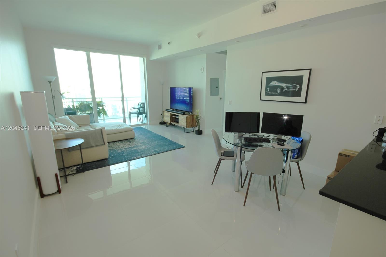 A bright living and dining area features white tile floors, a balcony, and modern furniture — 950 Brickell Bay Dr # 5000, Miami FL 33131, MIAMI, FL