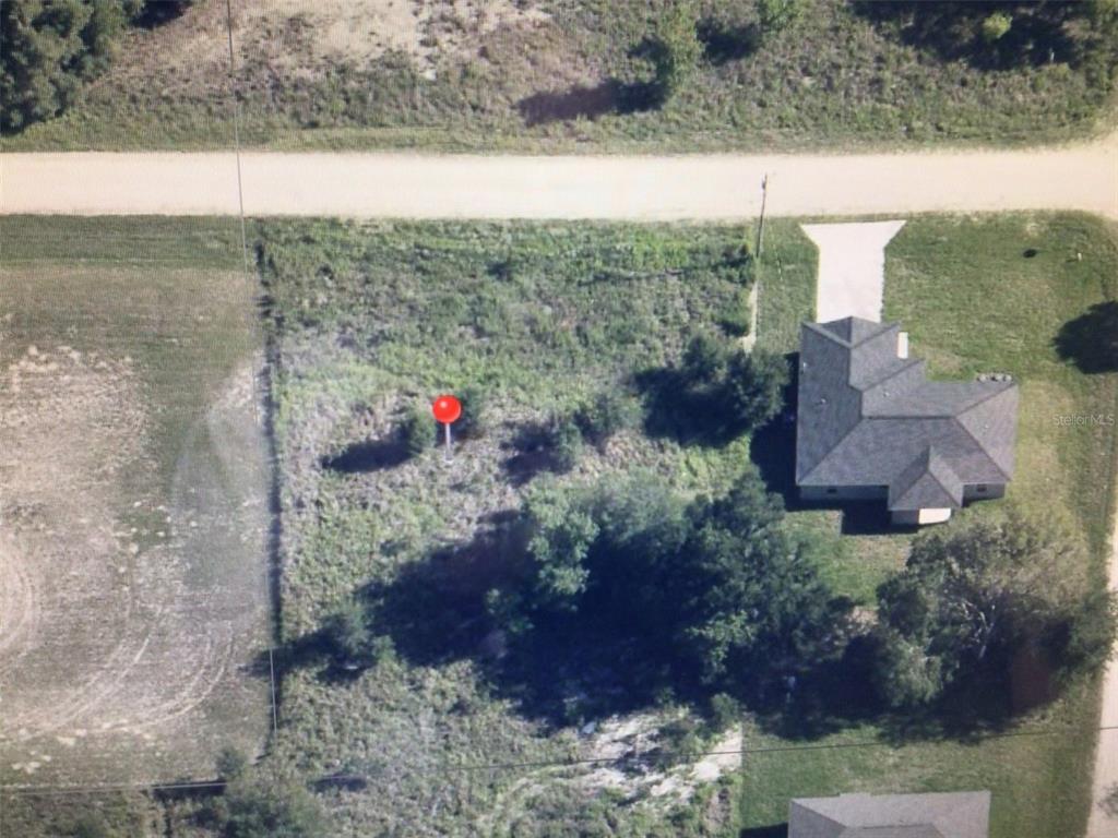 An aerial view shows a vacant, grass-covered residential lot next to an existing house — 0 SW 107 STREET, DUNNELLON, FL
