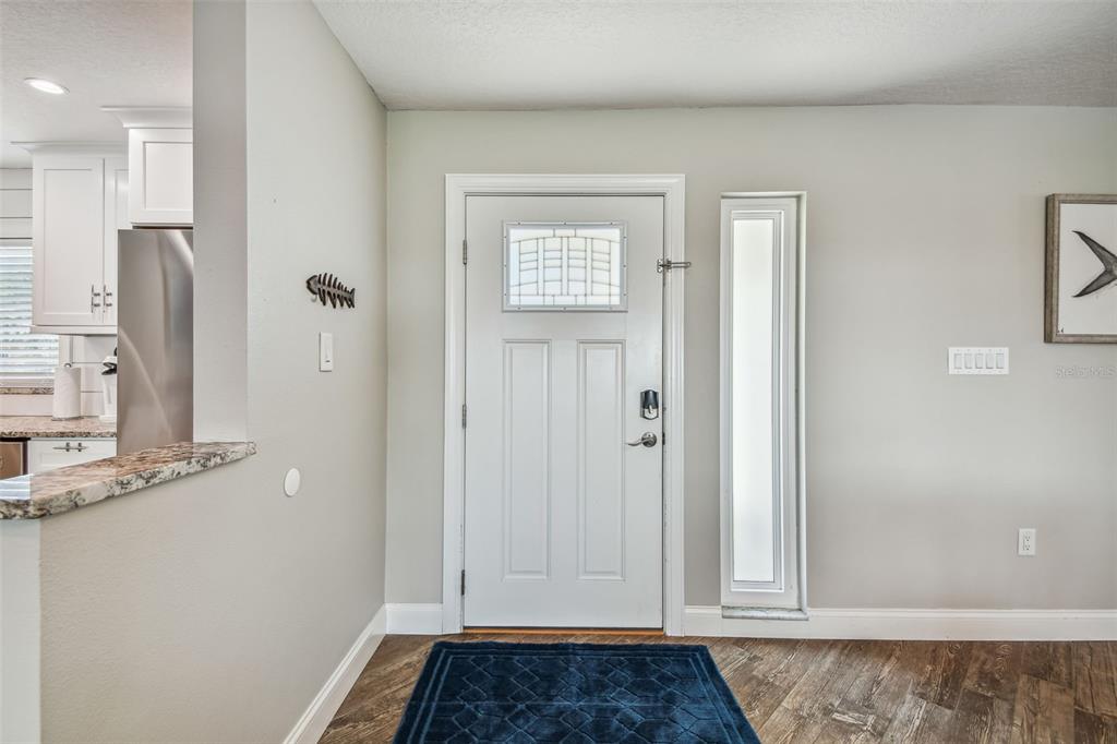 An entryway features a white front door with a sidelight, wood-look flooring, and a blue rug — 4900 ARLINGTON ROAD, PALMETTO, FL