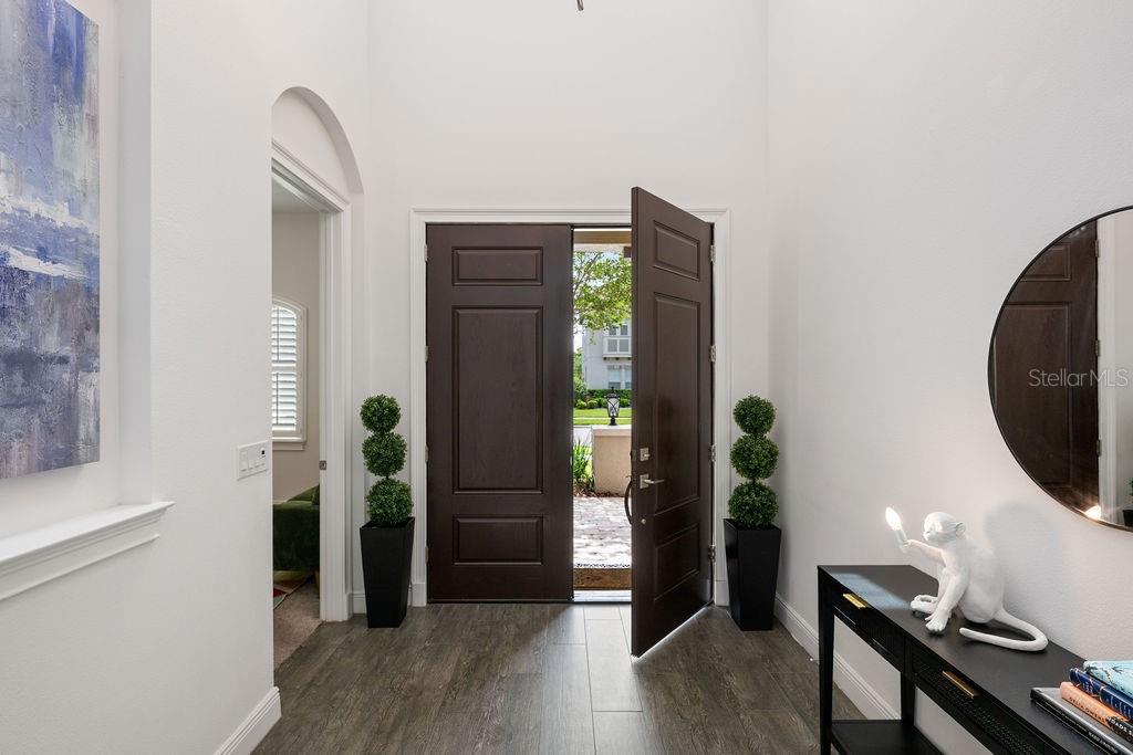 A bright entryway features dark wood double doors, gray wood-look flooring, and a console table — 706 CANOPY ESTATES DRIVE, WINTER GARDEN, FL