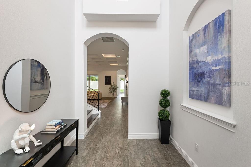 A bright entryway features a black console table, a round mirror, and a large wall painting — 706 CANOPY ESTATES DRIVE, WINTER GARDEN, FL