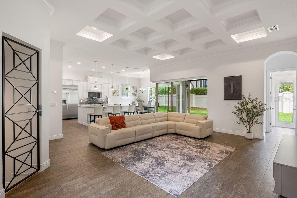 A bright open-concept living room with a coffered ceiling, large sectional sofa, and kitchen area — 706 CANOPY ESTATES DRIVE, WINTER GARDEN, FL