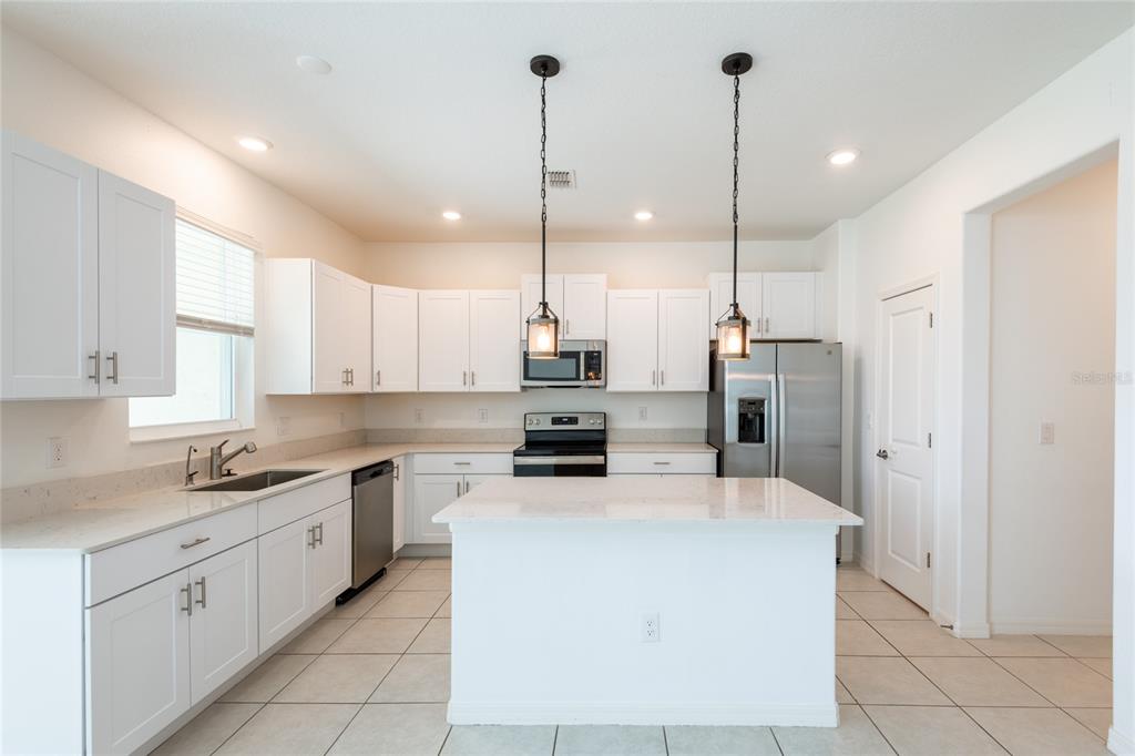 A kitchen features white cabinetry, stainless steel appliances, a center island, and tile flooring — 6262 SHINER STREET, LAND O LAKES, FL