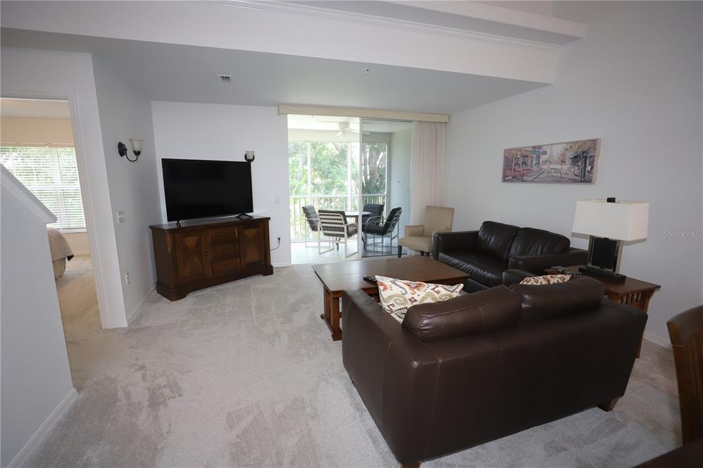 A living room features brown leather furniture, a wooden media console, and a screened balcony — 4275 CASTLEBRIDGE LANE UNIT 1323, SARASOTA, FL