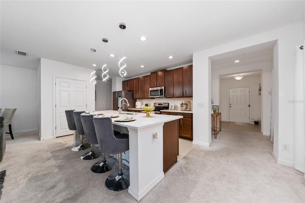 A kitchen features a white island with grey bar stools, dark wood cabinets, and pendant lighting — 669 JUPITER BEACH ROAD, GROVELAND, FL