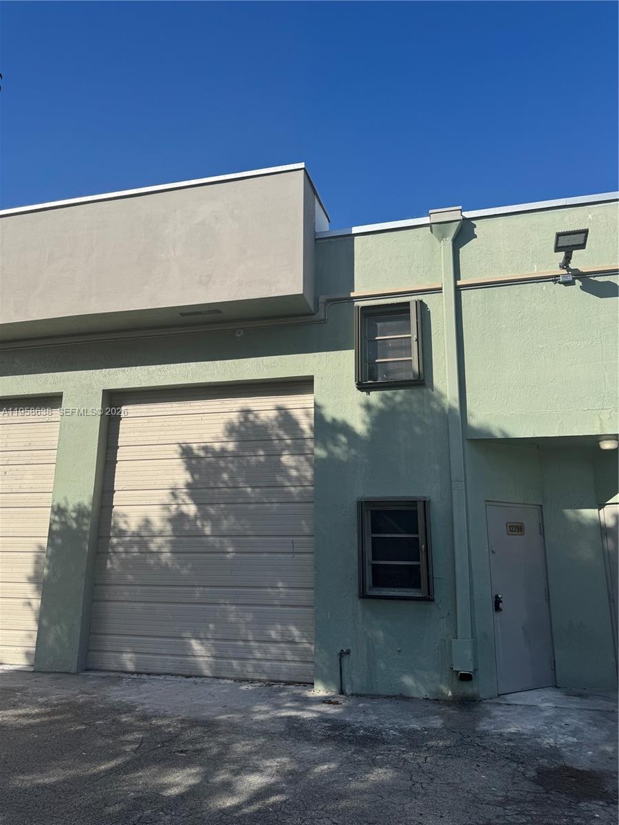 The exterior of a light green industrial building features a roll-up door and a pedestrian entrance — 12290 SW 131st Ave # 14, Miami FL 33186, MIAMI, FL