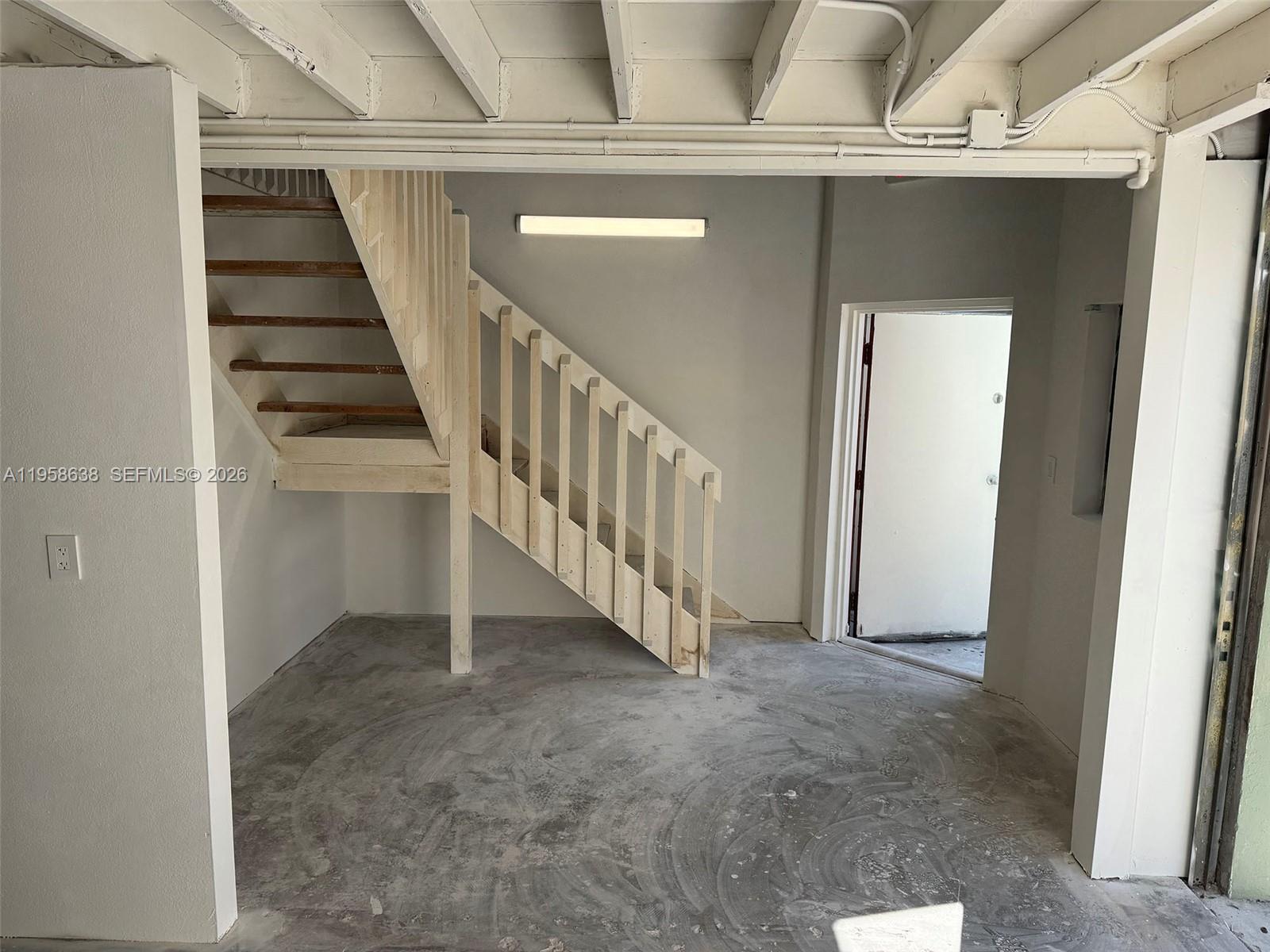 An unfinished room features a wooden staircase, concrete flooring, and an open doorway — 12290 SW 131st Ave # 14, Miami FL 33186, MIAMI, FL