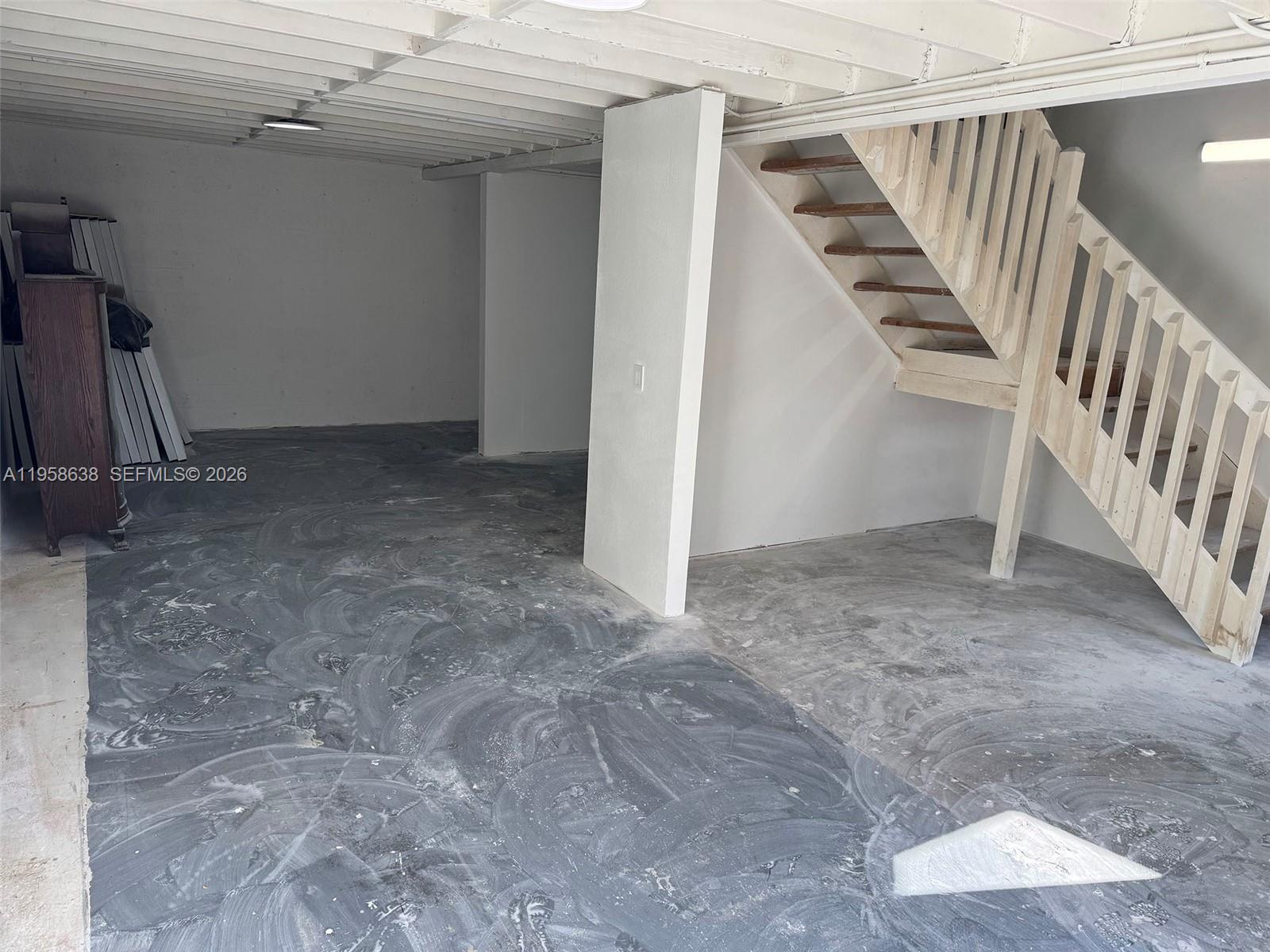 An unfinished basement features a concrete floor, white walls, and an exposed wooden staircase — 12290 SW 131st Ave # 14, Miami FL 33186, MIAMI, FL