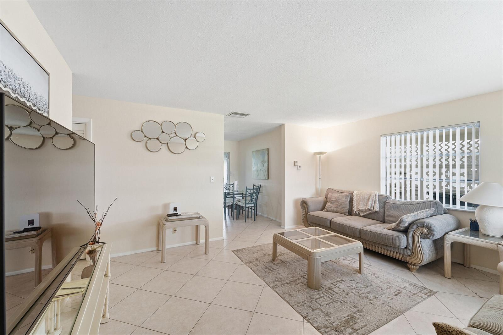 A living room with tile floors, a gray sofa, a coffee table, and a dining area — 220 Leisure Boulevard, Pompano Beach FL 33064, POMPANO BEACH, FL