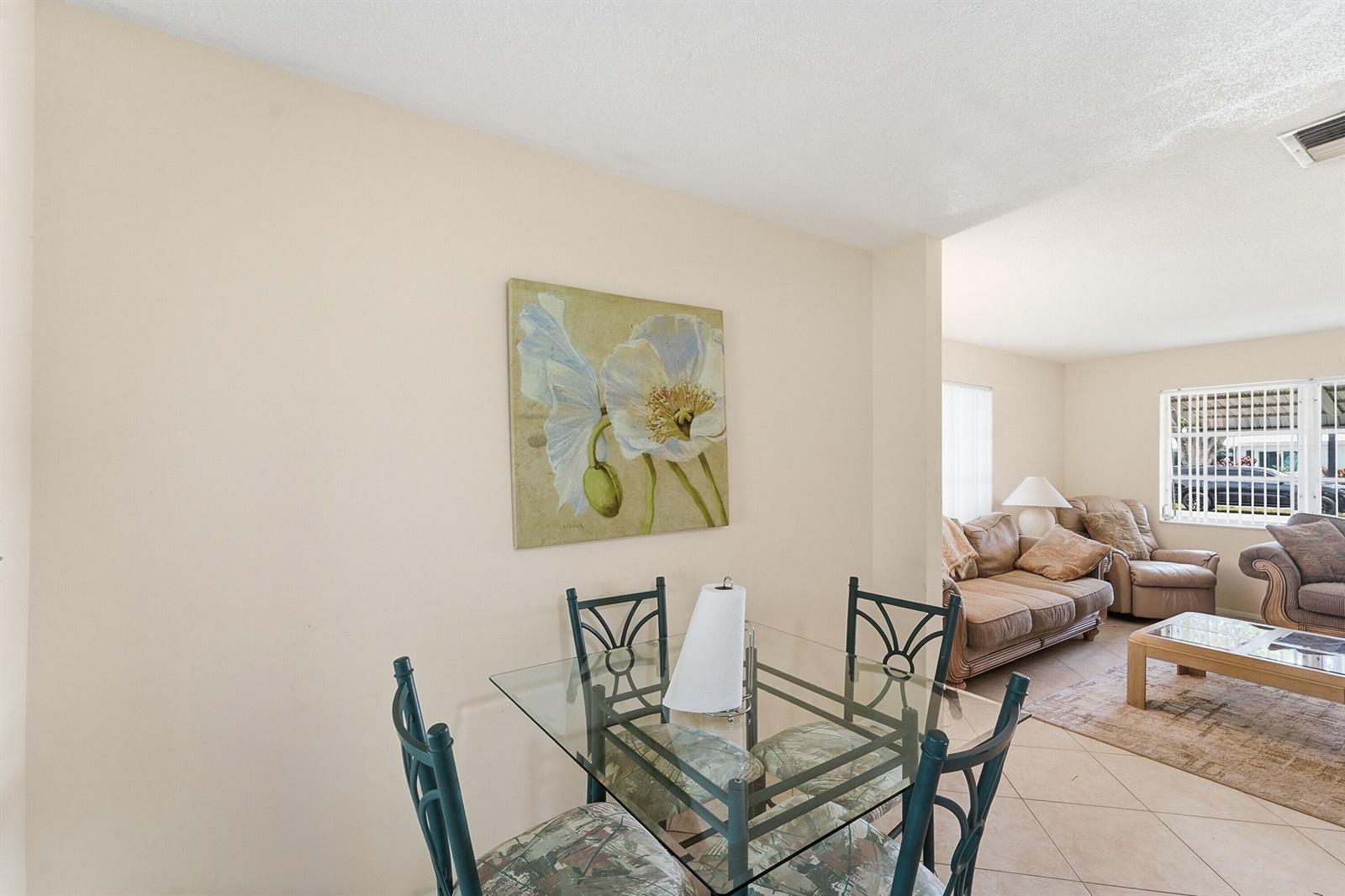 A dining area with a glass table and chairs sits adjacent to a living room — 220 Leisure Boulevard, Pompano Beach FL 33064, POMPANO BEACH, FL
