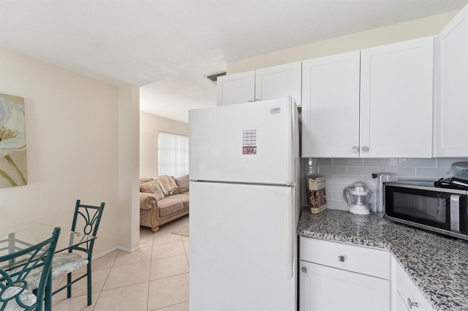 A kitchen with white cabinets, granite countertops, and a refrigerator opens to a dining area — 220 Leisure Boulevard, Pompano Beach FL 33064, POMPANO BEACH, FL