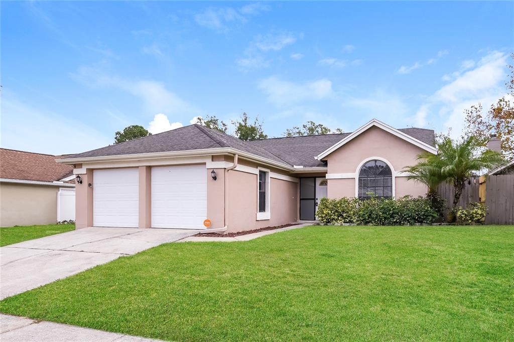A single-story house with a two-car garage, beige stucco exterior, and a front lawn — 1961 MARTINA STREET, APOPKA, FL