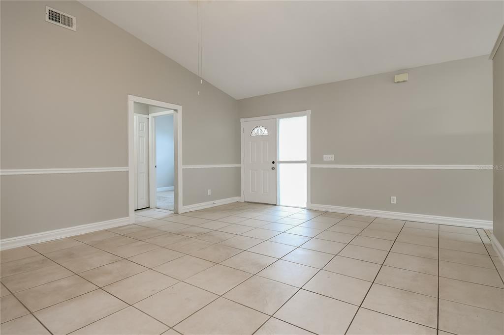 An empty living room features light gray walls, white trim, and beige tiled flooring — 1961 MARTINA STREET, APOPKA, FL