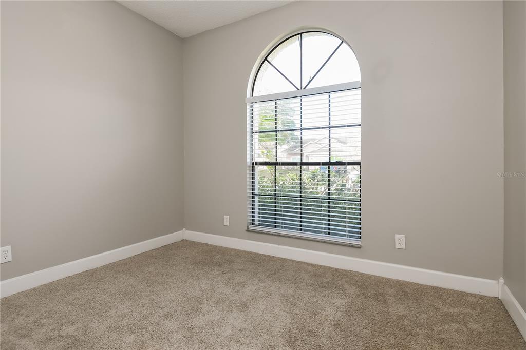 An empty room features beige carpet, light gray walls, and a large arched window — 1961 MARTINA STREET, APOPKA, FL