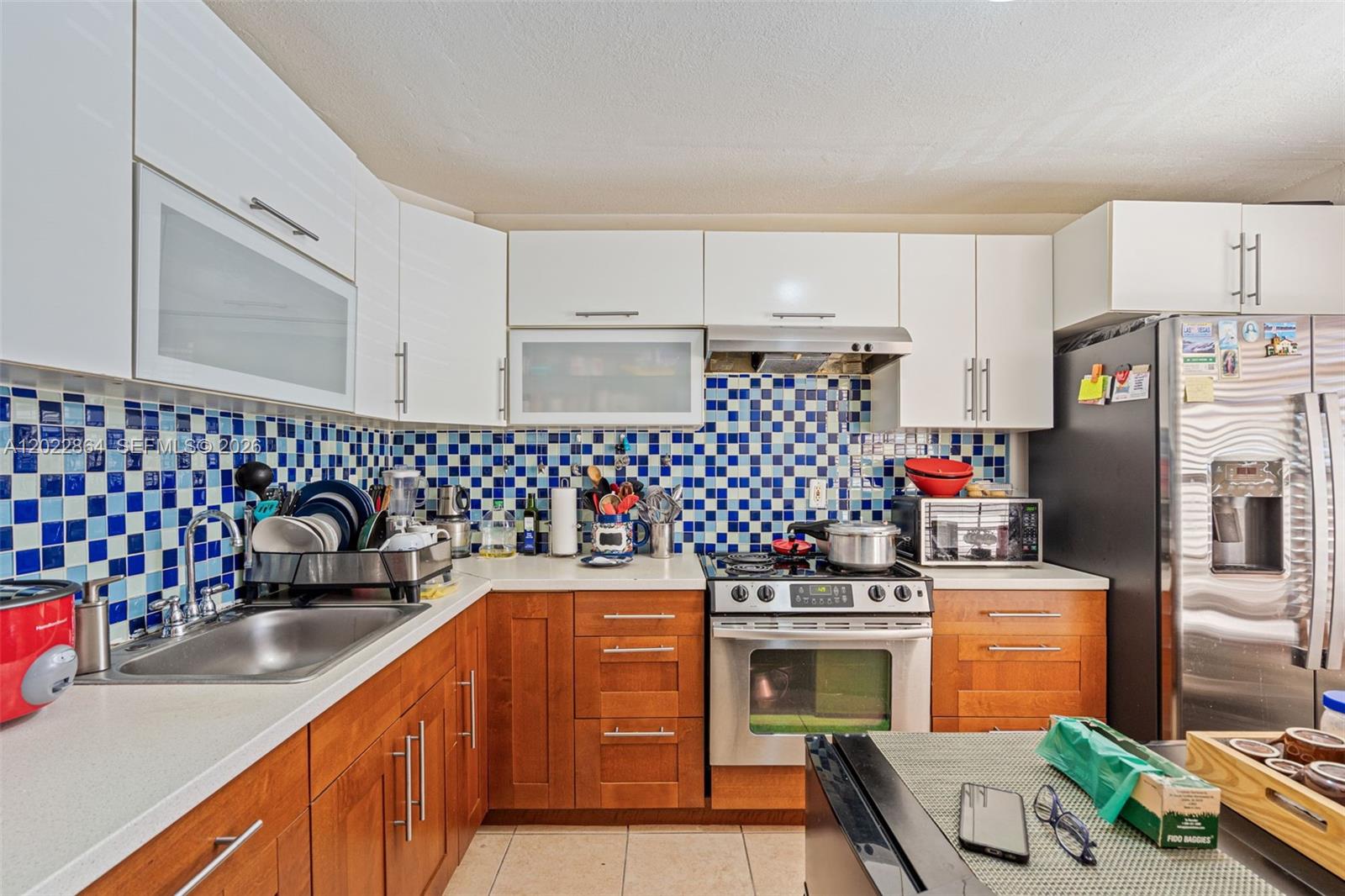 A kitchen features white upper cabinets, wood lower cabinets, and a blue tiled backsplash — 12927 SW 88th Ln # A205, Miami FL 33186, MIAMI, FL