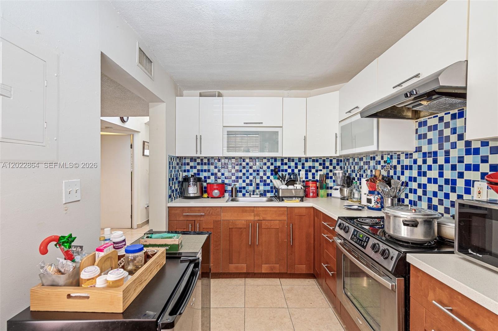 A kitchen features wood lower cabinets, white upper cabinets, and a blue-and-white tiled backsplash — 12927 SW 88th Ln # A205, Miami FL 33186, MIAMI, FL