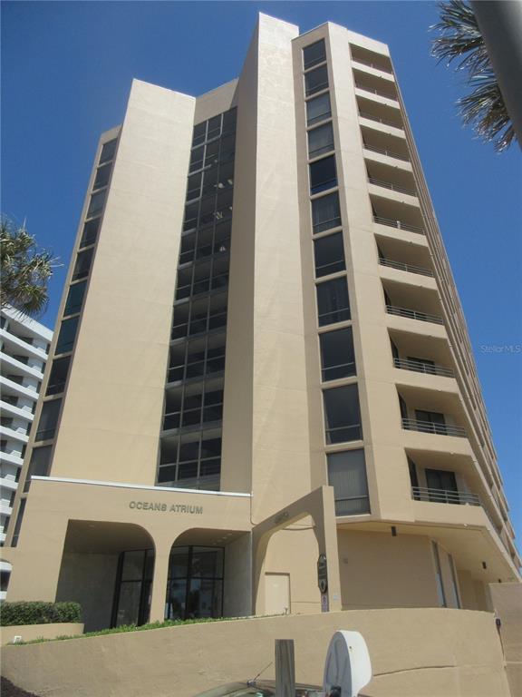 A low-angle view of the tan, multi-story Oceans Atrium condominium building against a blue sky — 3023 S ATLANTIC AVENUE UNIT 2070, DAYTONA BEACH, FL