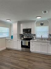 A kitchen features white cabinets, stainless steel appliances, and wood-look flooring — 16931 FRANKLIN AVENUE, MONTVERDE, FL