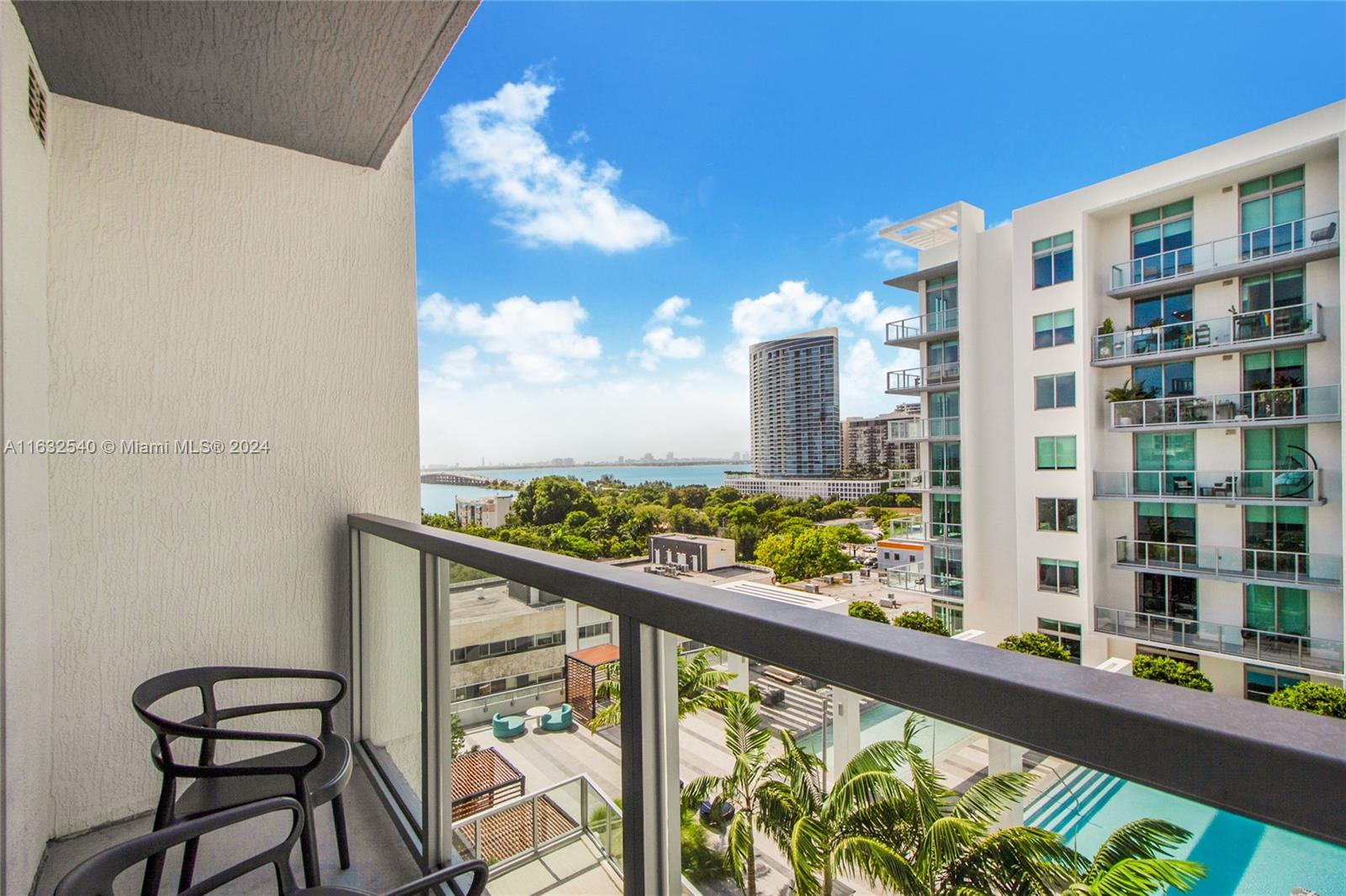 A balcony view overlooks a swimming pool, palm trees, and a distant city skyline — 3900 Biscayne Blvd # 917, Miami FL 33137, MIAMI, FL