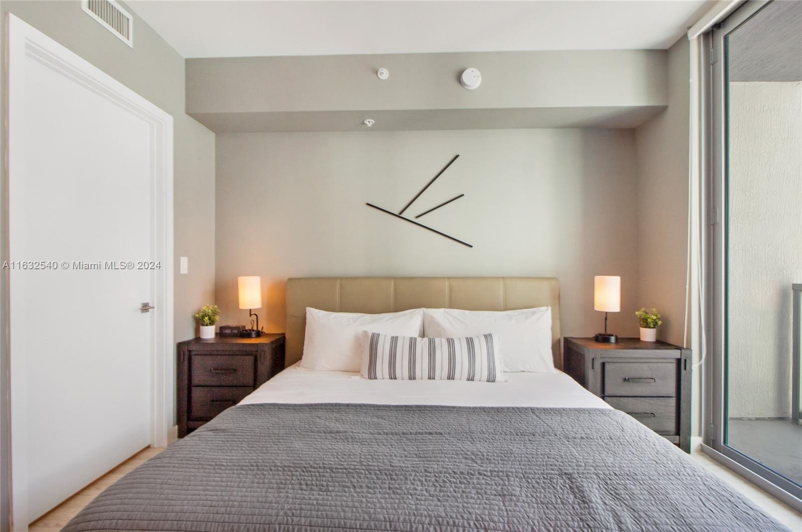 A bedroom features a bed with a tan headboard, two dark nightstands, and a balcony door — 3900 Biscayne Blvd # 917, Miami FL 33137, MIAMI, FL