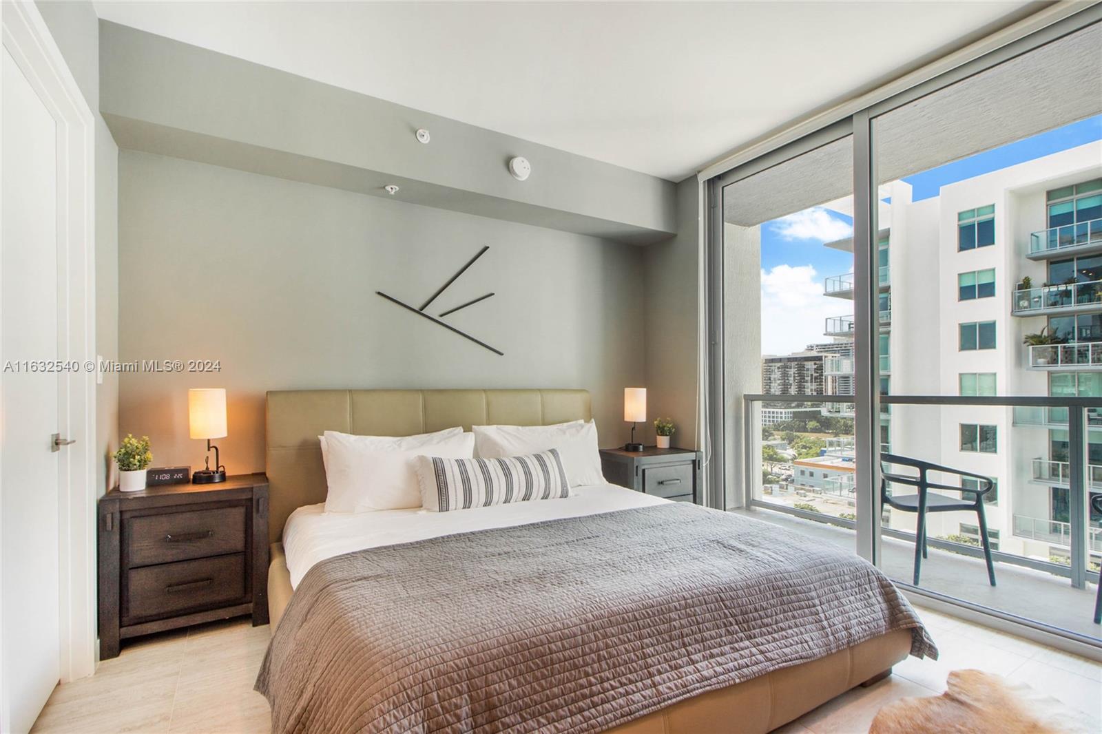 A bedroom features a bed with a gray quilt, two nightstands, and a balcony view — 3900 Biscayne Blvd # 917, Miami FL 33137, MIAMI, FL