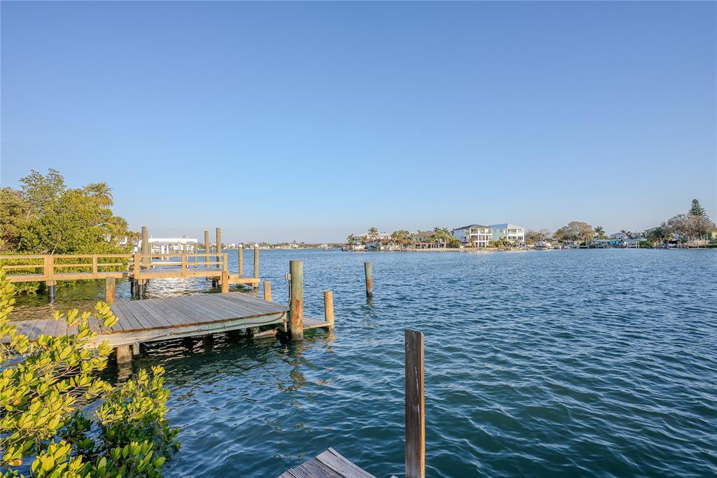 A wooden dock extends into a calm waterway with houses visible on the distant shore — 407 20TH AVENUE, INDIAN ROCKS BEACH, FL