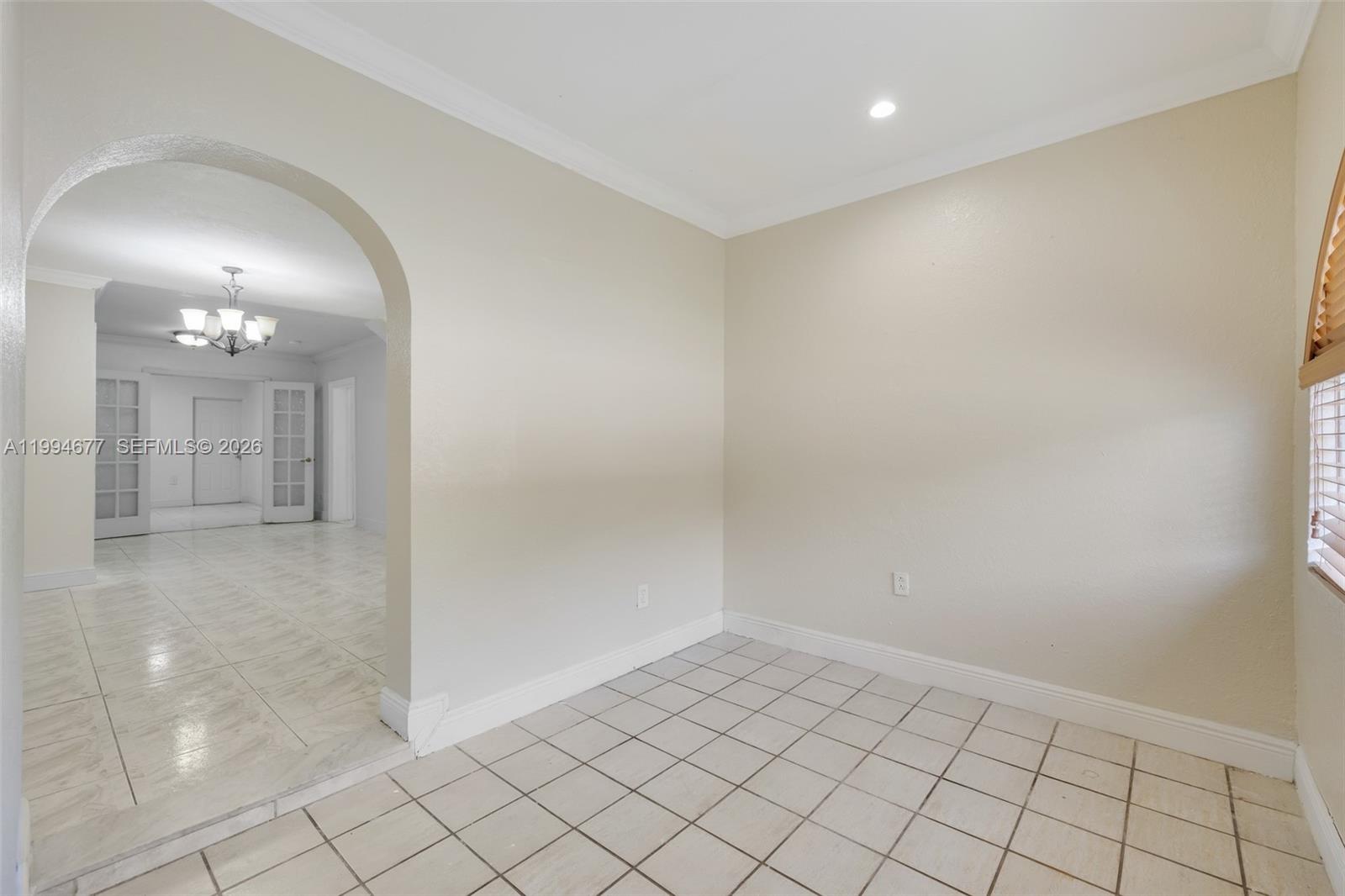 An empty room with beige walls, white tile flooring, and an arched entryway — 674 W 23rd St, Hialeah FL 33010, HIALEAH, FL