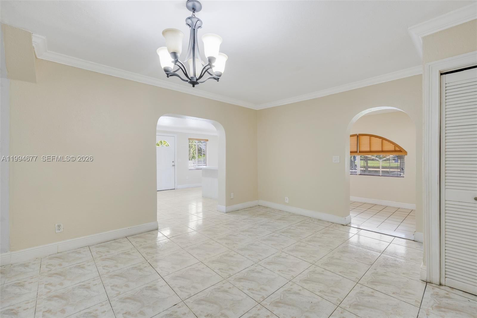 A dining room with beige walls, tile flooring, a chandelier, and two arched doorways — 674 W 23rd St, Hialeah FL 33010, HIALEAH, FL