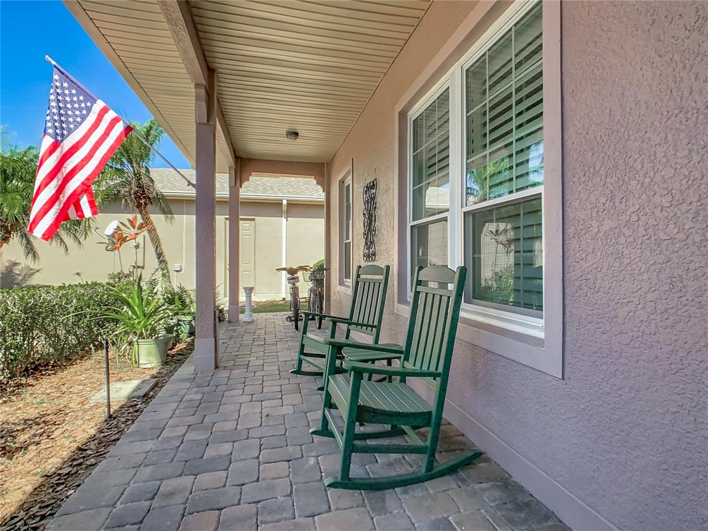 A covered front porch features brick pavers, two green rocking chairs, and an American flag — 1155 N GLENDORA ROAD, KISSIMMEE, FL
