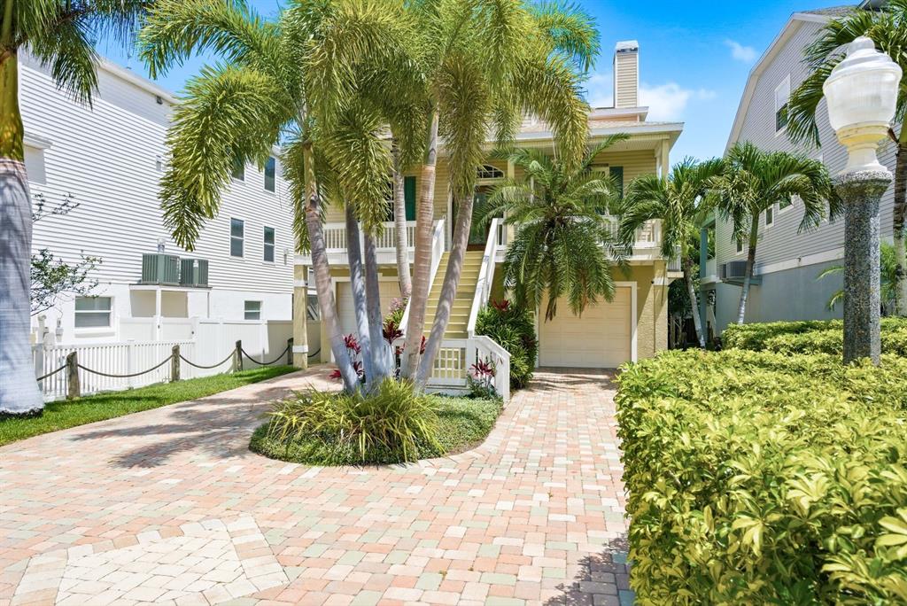 A yellow elevated house with a paver driveway, palm trees, and a white picket fence — 503 PALM AVENUE, PALM HARBOR, FL