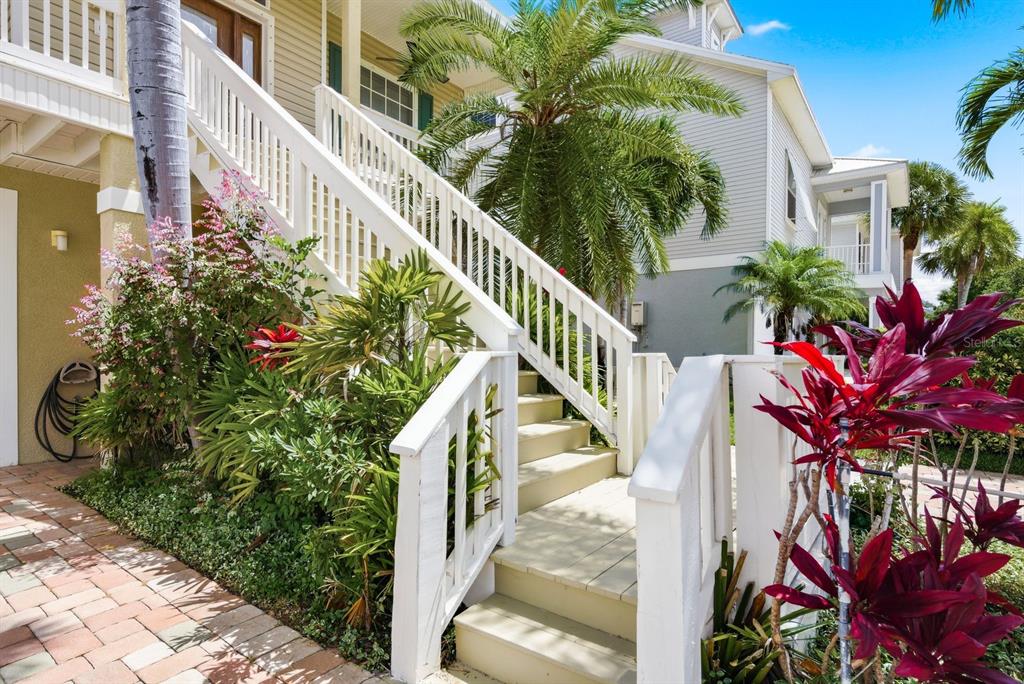 Exterior stairs with white railings lead to a raised entrance surrounded by tropical landscaping — 503 PALM AVENUE, PALM HARBOR, FL