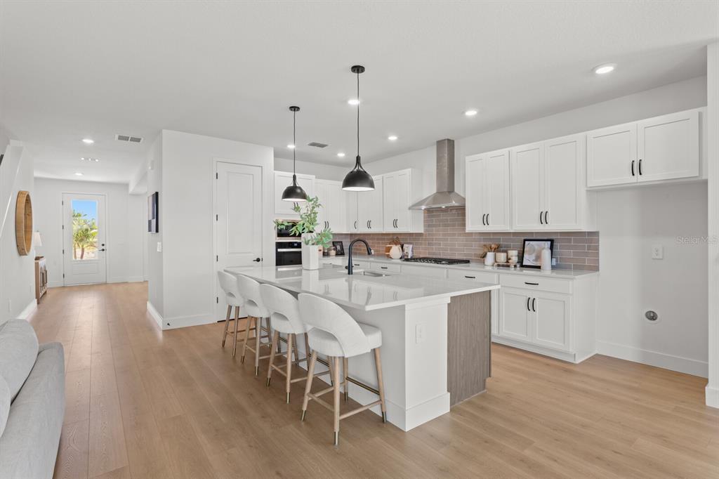 A modern kitchen features white cabinetry, a large island with bar seating, and wood flooring — 7770 OCEAN SPRAY TRAIL, PALMETTO, FL