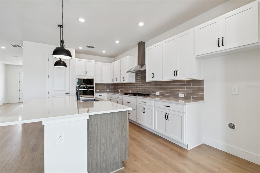 A modern kitchen features white cabinets, a gray tiled backsplash, and a large center island — 7770 OCEAN SPRAY TRAIL, PALMETTO, FL