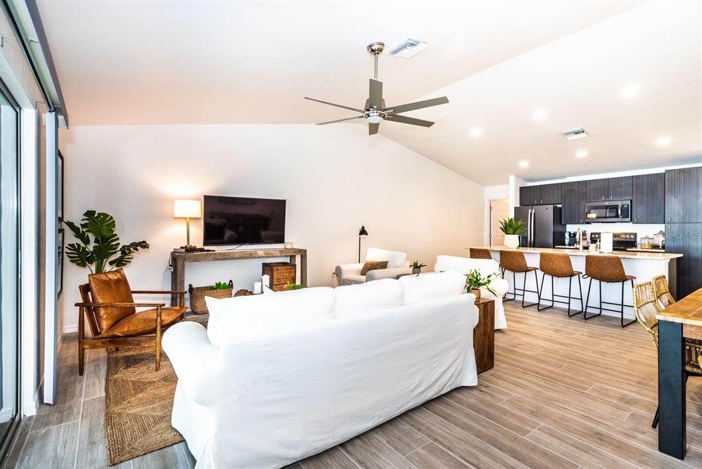 An open-concept living room and kitchen featuring a white sofa, leather chairs, and wood flooring — 215 LEWIS CIRCLE UNIT 111, PUNTA GORDA, FL