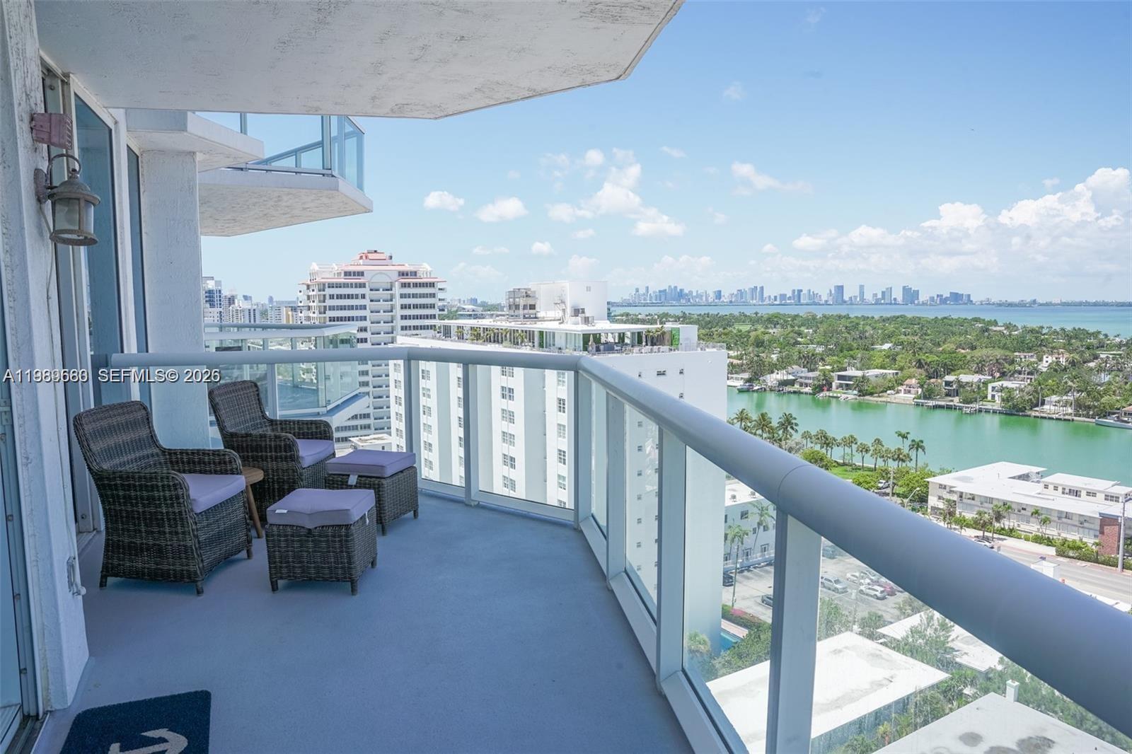 A high-rise balcony features wicker chairs and a glass railing overlooking a bay — 6515 Collins Ave # 1709, Miami Beach FL 33141, MIAMI BEACH, FL